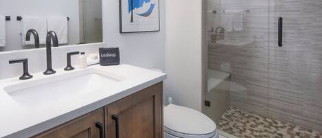 Ein modernes Badezimmer mit einem weißen Waschbecken, dunklen Holzschränken, einer Toilette und einer gläsernen Duschkabine.