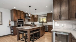 Une cuisine moderne avec des meubles en bois, un îlot central doté de tabourets de bar, des appareils en acier inoxydable et un éclairage suspendu.
