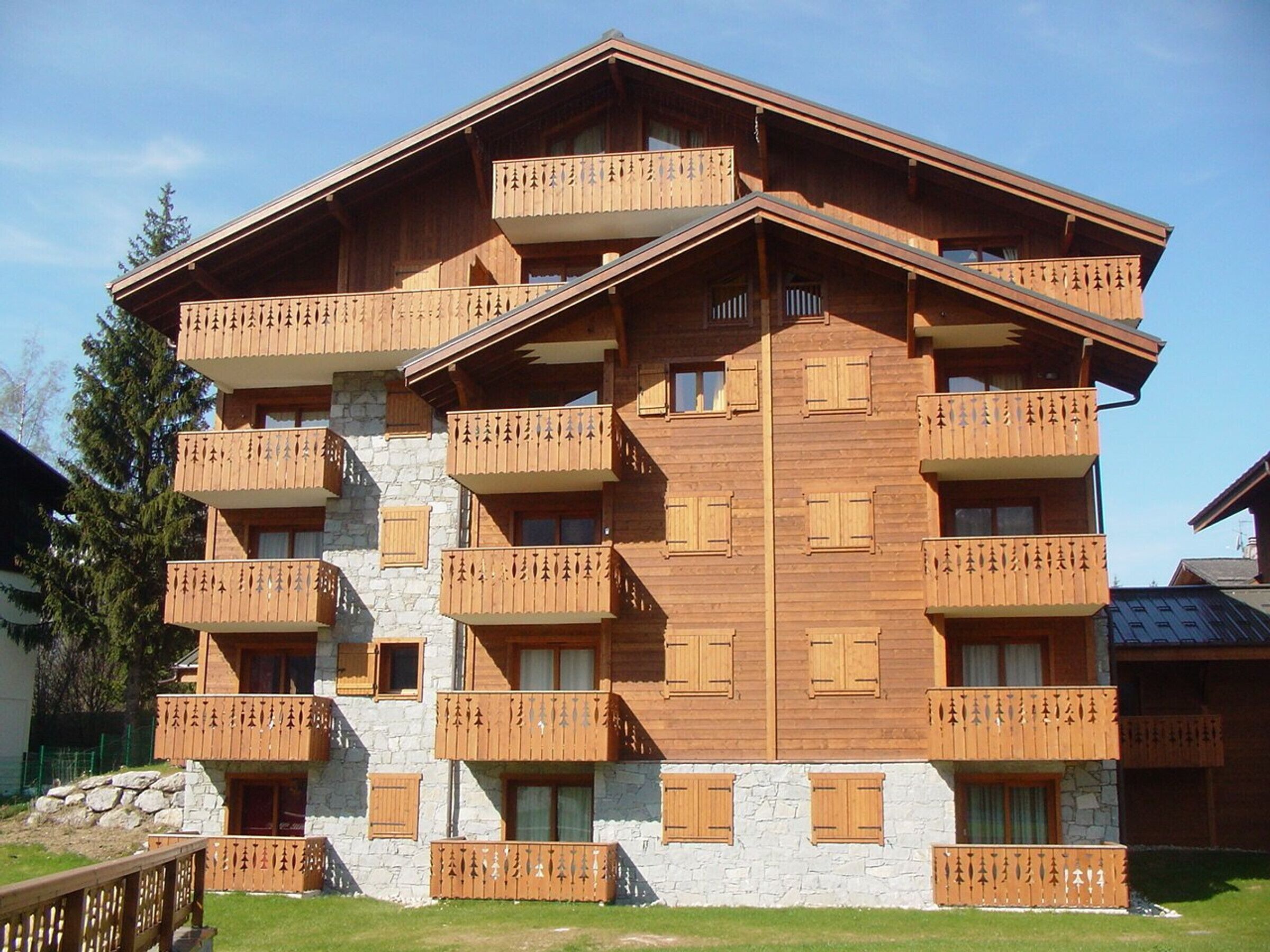 Un immeuble en bois à plusieurs étages, doté de balcons et d’une façade en pierre, avec un ciel dégagé.