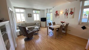 Ein modernes Wohnzimmer mit einer Couch, Sesseln, einem Esstisch und einem Fernseher.