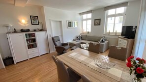 Un salon moderne comprenant un canapé, une table à manger avec des chaises, un téléviseur et une bibliothèque.