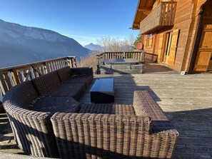 A wooden deck with wicker furniture, a hot tub, and a view of mountains.