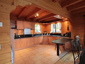 A wooden cabin kitchen with a central island, built-in cabinets, and a window with curtains.