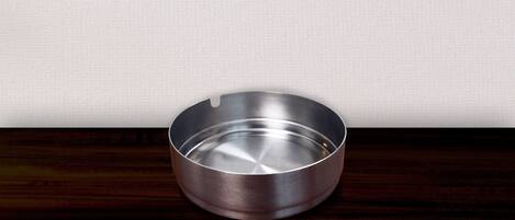 A metallic ashtray on a wooden surface against a plain wall.