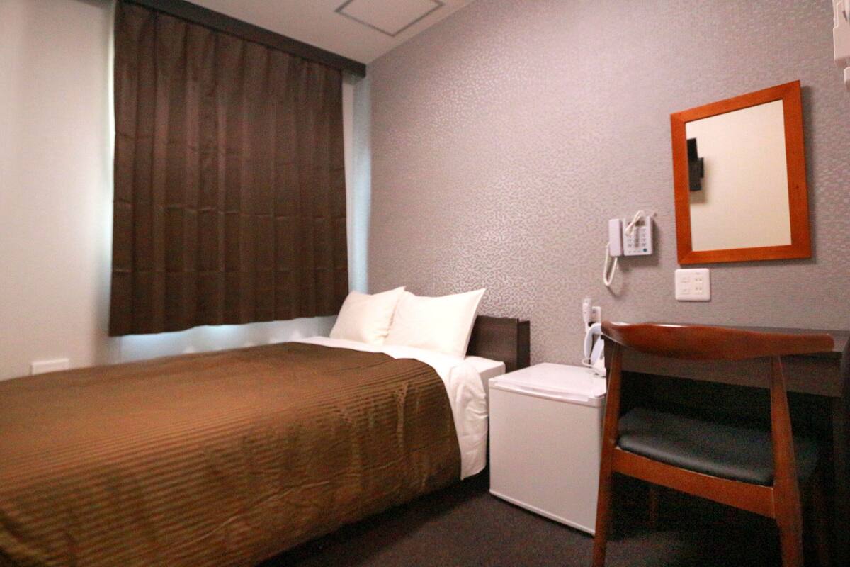 Une chambre d’hôtel équipée d’un lit, d’un bureau, d’une chaise, d’un téléphone et d’une fenêtre avec des rideaux.