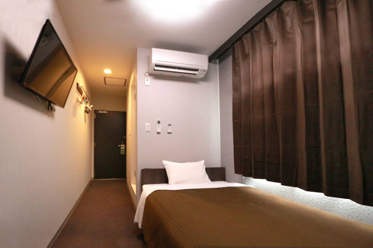 Une chambre d’hôtel équipée d’un lit, d’un climatiseur, d’un téléviseur fixé au mur et d’une fenêtre avec des rideaux.