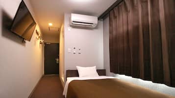 Une chambre d’hôtel équipée d’un lit, d’un climatiseur, d’un téléviseur fixé au mur et d’une fenêtre avec des rideaux.