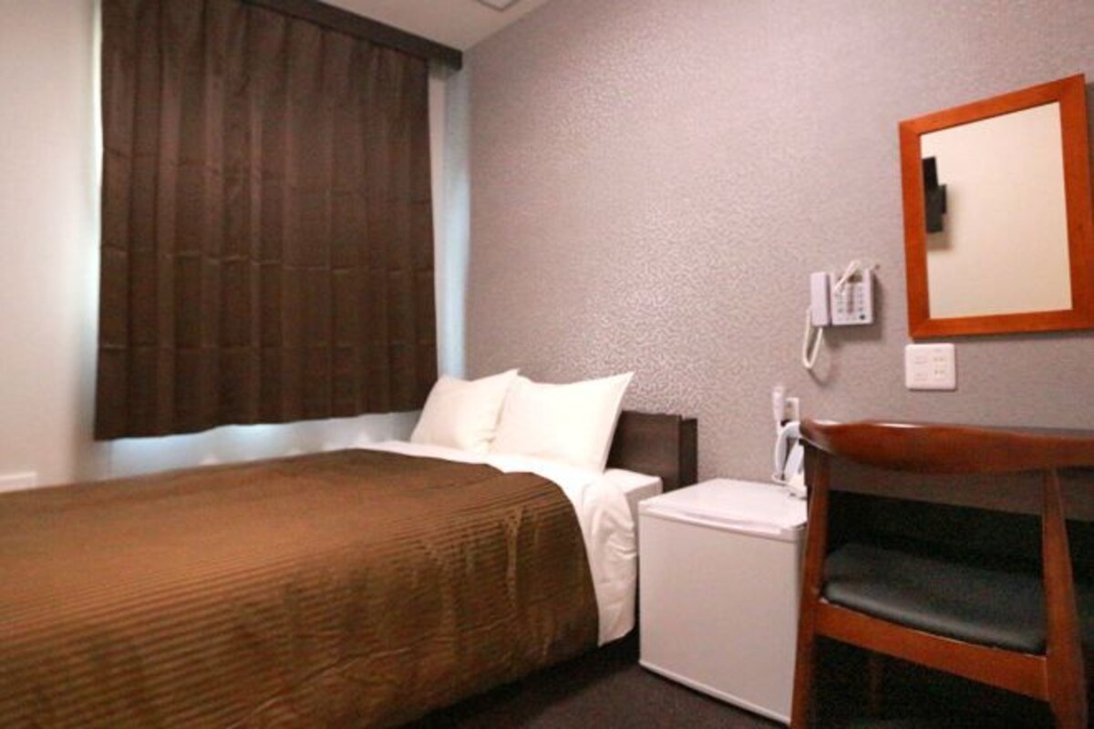 Een hotelkamer met een bed, een nachtkastje, een stoel, een spiegel en een telefoon.