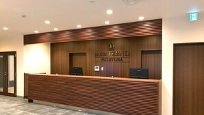 Ein Empfangsschalter mit Holzoptik und einem Schild mit der Aufschrift 'HOTEL TREND FUKUYAMA'.