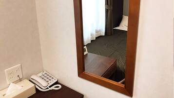 Camera d'albergo con uno specchio con cornice in legno, un telefono sul comodino e un astuccio per fazzoletti su un tavolino.
