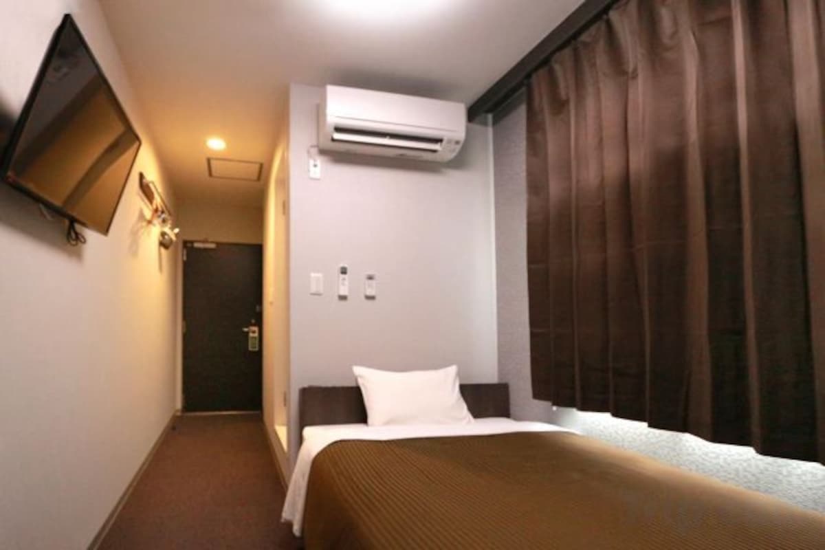Une chambre d’hôtel comprenant un lit, un climatiseur fixé au mur, une télévision et une porte donnant sur une autre pièce.