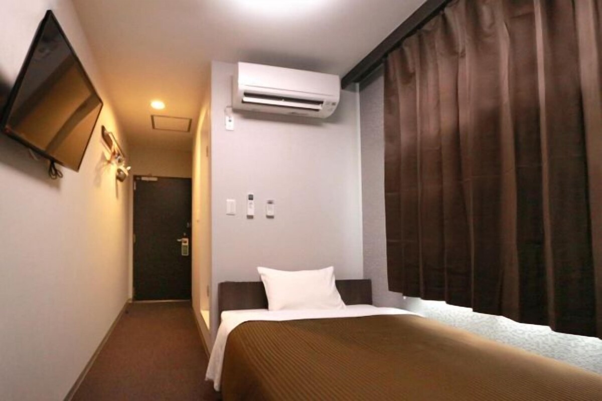 Ein Hotelzimmer mit einem Bett, einer Klimaanlage, einem an der Wand befestigten Flachbildfernseher und einer Tür am Ende des Flurs.