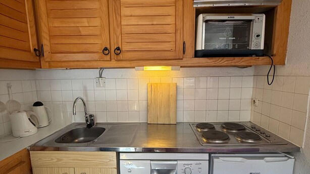 A compact kitchen with wooden cabinets, a microwave, a dishwasher, and a stove.