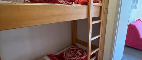 Un lit superposé avec une échelle, une couverture à motifs rouges et blancs, et un coussin rouge.