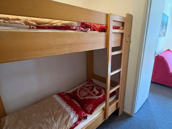 Una cama litera con escalera, una colcha roja y blanca estampada, y un cojín rojo.