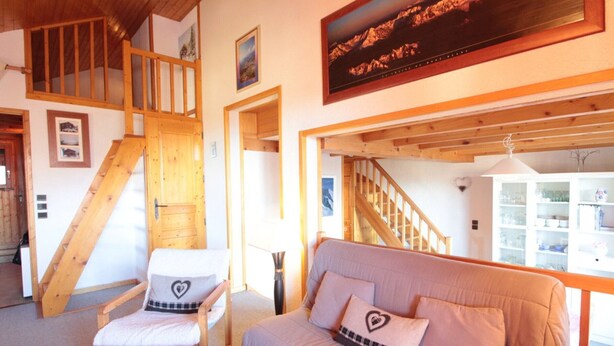 Ein gemütliches Zimmer mit einer Holztreppe, einem gepolsterten Sofa mit Herzmustern und einem Holztisch.