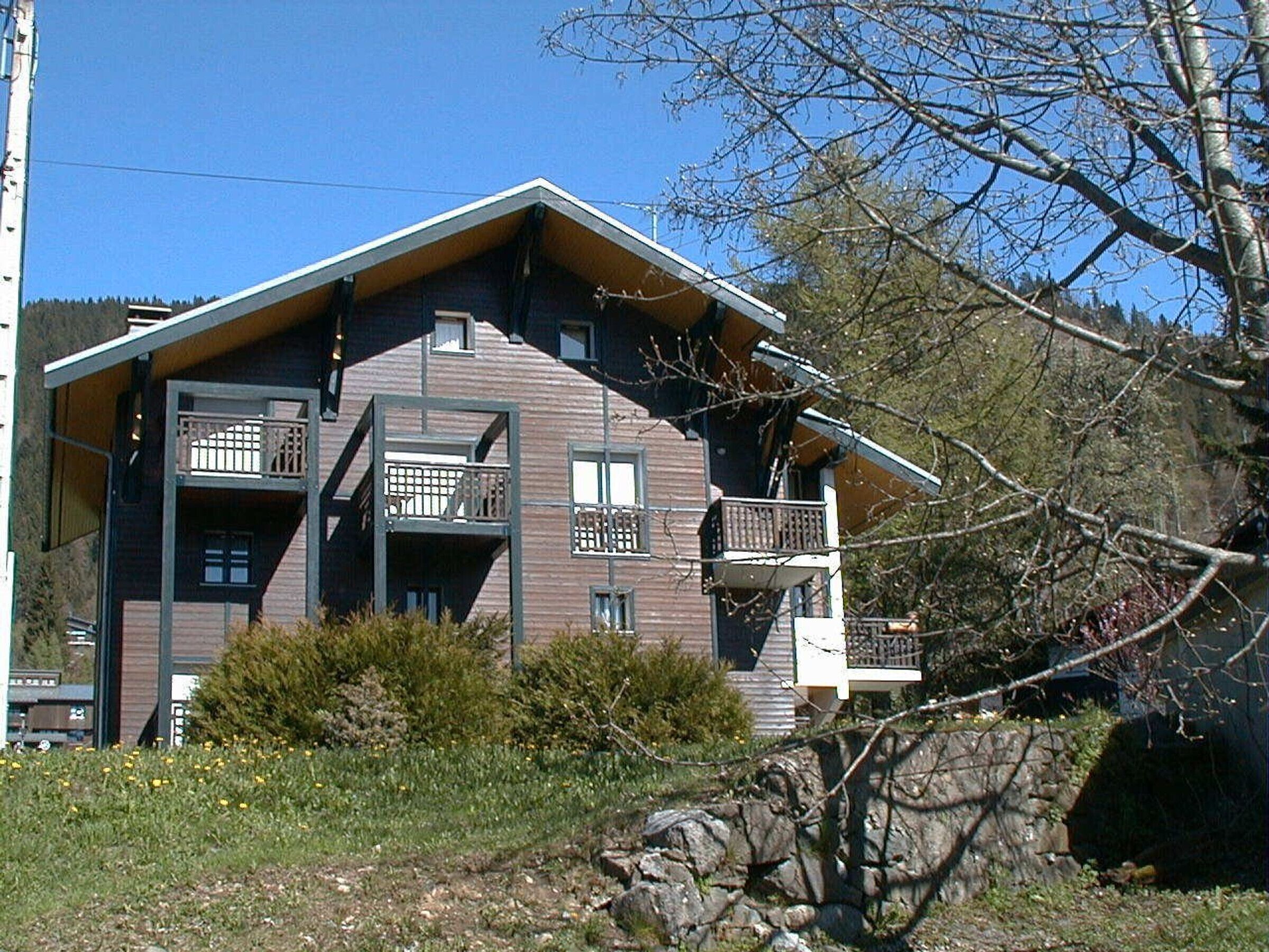 A multi-story building with balconies, a stone wall, and a clear sky.