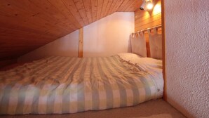 Ein kleines Schlafzimmer im Dachgeschoss mit schrägen Wänden, einem Einzelbett und einer Wandleuchte.