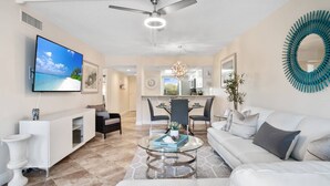 A modern living room with a TV, sofa, coffee table, and dining area. - Updated w/Exterior Entry; Walk to Beaches ~In-Unit Laundry & WiFi w/Grill, Pool/Spa & Tennis (Marco Island)