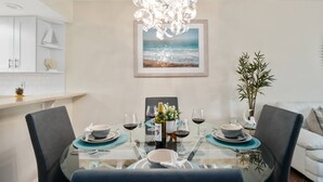A dining area with a glass table, chairs, and a chandelier. There is a framed picture of a beach on the wall. - Updated w/Exterior Entry; Walk to Beaches ~In-Unit Laundry & WiFi w/Grill, Pool/Spa & Tennis (Marco Island)