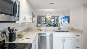A modern kitchen with white cabinets, stainless steel appliances, and a central island with seating. - Updated w/Exterior Entry; Walk to Beaches ~In-Unit Laundry & WiFi w/Grill, Pool/Spa & Tennis (Marco Island)