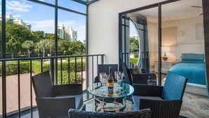 A balcony with wicker furniture, a glass table, and a bottle of wine. - Updated w/Exterior Entry; Walk to Beaches ~In-Unit Laundry & WiFi w/Grill, Pool/Spa & Tennis (Marco Island)