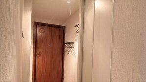 En hall med en trädörr, en väggmonterad hylla och ett golv täckt av en matta.