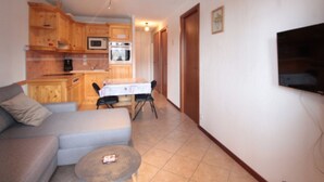 Ett kompakt bostadsutrymme med ett litet pentry, en soffa, ett litet runt bord och en TV som är monterad på väggen.