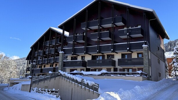 Ett hotell med flera våningar, balkonger, ett snötäckt område och en klarblå himmel.
