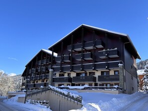 A multi-story hotel with balconies, a snow-covered ground, and a clear blue sky.