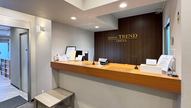 A hotel reception desk with a wooden counter, a reception area, and a door leading to the hallway. - Hotel Trend Omiya (Saitama)
