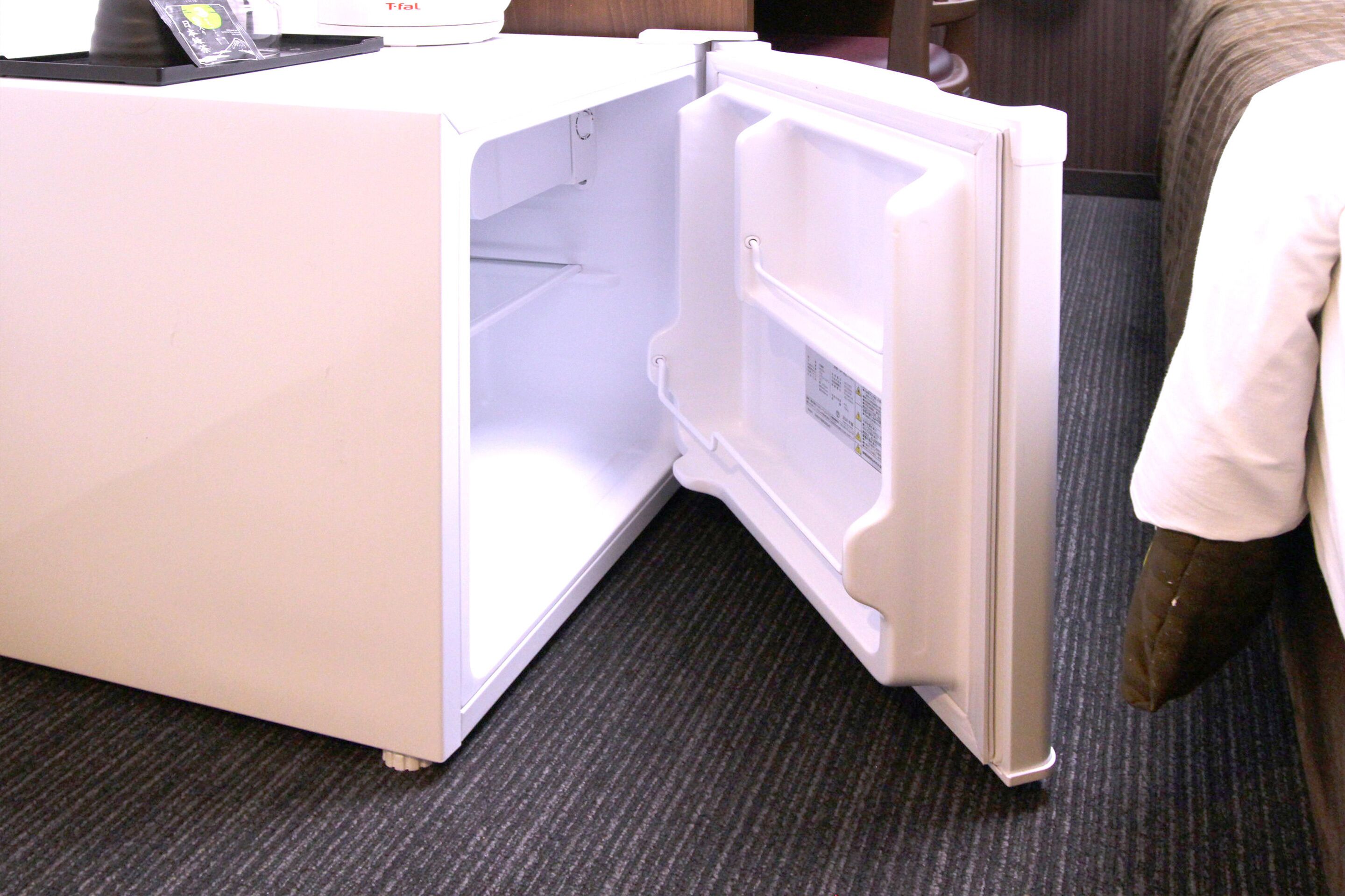 A white refrigerator with a freezer compartment, located in a room with a carpeted floor.