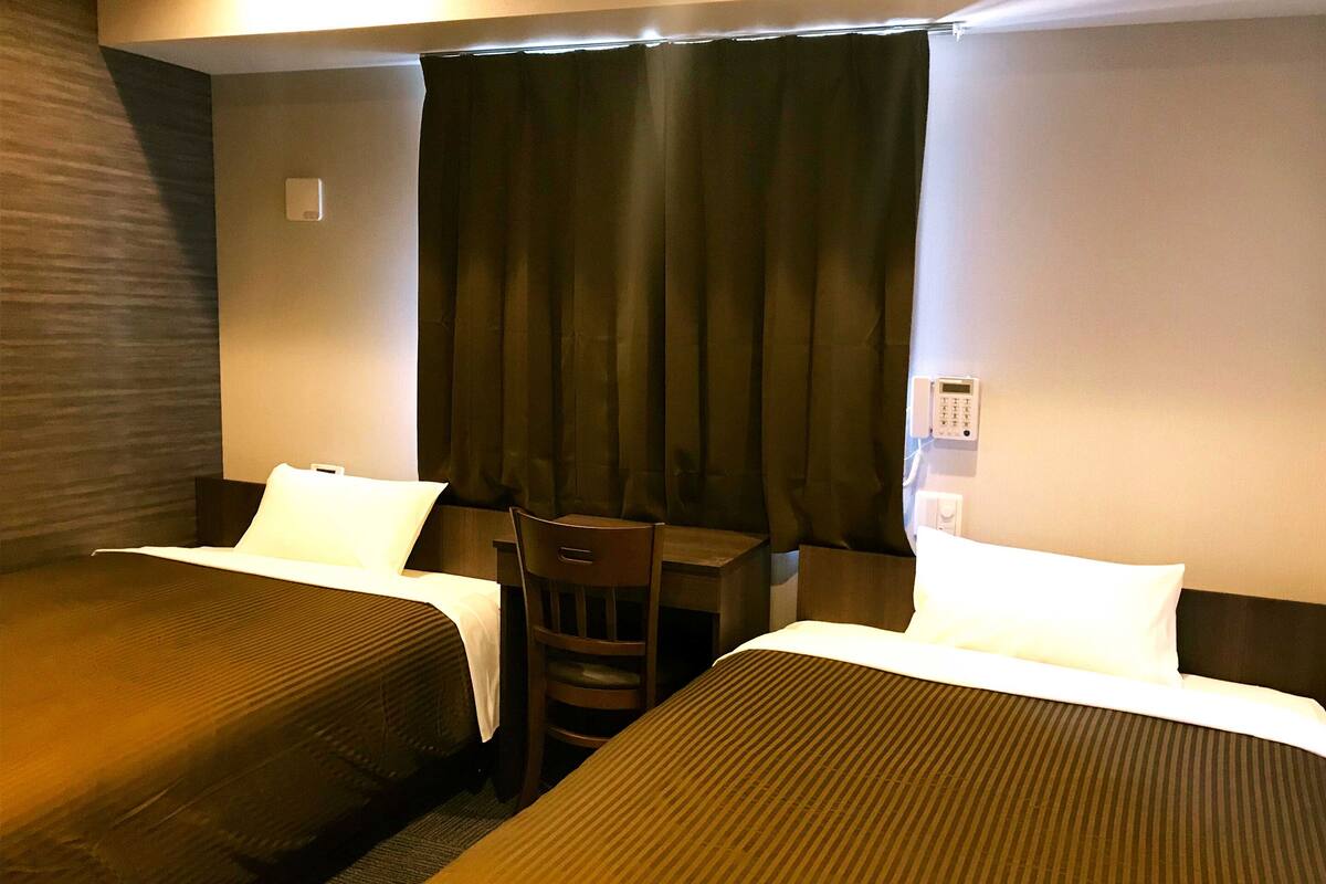 A hotel room with two beds, a desk, and a chair.
