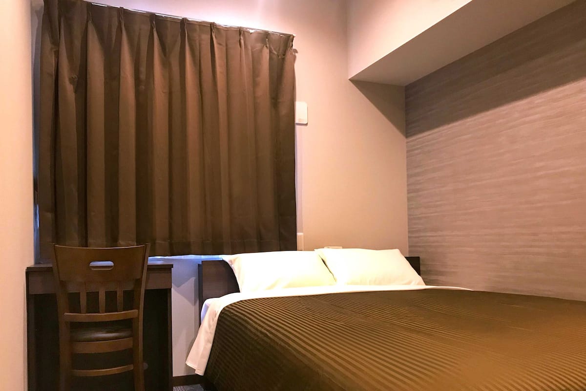 A hotel room with a bed, a chair, and a window with curtains.