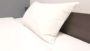 A neatly made bed with a white pillow and a dark wooden headboard. - Hotel Trend Omiya (Saitama)
