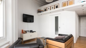A modern living room with a sofa, a TV, a cabinet, and a door. - Immaculate 1-bed Apartment on Hove Seafront (Hove)