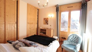 A bedroom with a bed, a chair, a dresser, a chandelier, and a window with curtains. - 3-bedroom apartment, 2 bathrooms, parking, near slopes, equipped with high standards (Les Carroz d'Arâches)