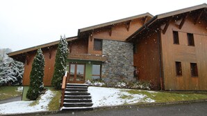 A modern building with a stone facade, wooden exterior, and a green entrance. - 3-bedroom apartment, 2 bathrooms, parking, near slopes, equipped with high standards (Les Carroz d'Arâches)