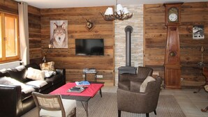 A living room with a fireplace, a television, a sofa, a chair, and a clock on the wall. - 3-bedroom apartment, 2 bathrooms, parking, near slopes, equipped with high standards (Les Carroz d'Arâches)