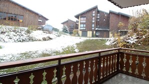 A balcony with a metal railing overlooking a courtyard with snow-covered ground and buildings in the background. - 3-bedroom apartment, 2 bathrooms, parking, near slopes, equipped with high standards (Les Carroz d'Arâches)