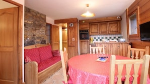 A cozy kitchen with wooden cabinets, a stone wall, a red sofa, and a dining table with chairs. - 3-room cabin apartment with parking, near slopes and shops (Les Carroz d'Arâches)
