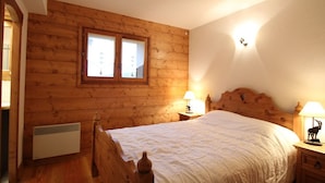 A wooden-paneled bedroom with a bed, two bedside lamps, and a window. - 3-room cabin apartment with parking, near slopes and shops (Les Carroz d'Arâches)