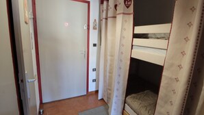 A bedroom with a bunk bed, a door with a red frame, and curtains with heart patterns.