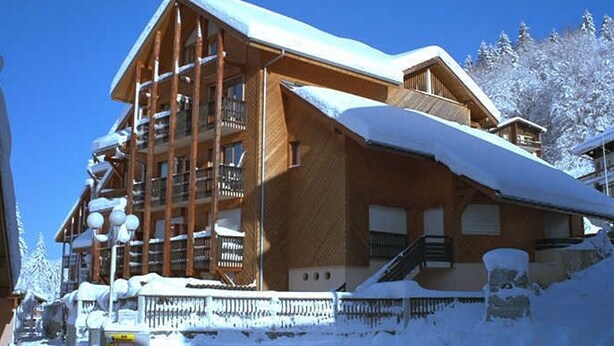 A wooden chalet with a sloped roof, multiple balconies, and a snow-covered exterior.