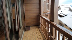 A balcony with wooden railings and a tiled floor, overlooking a snowy landscape.