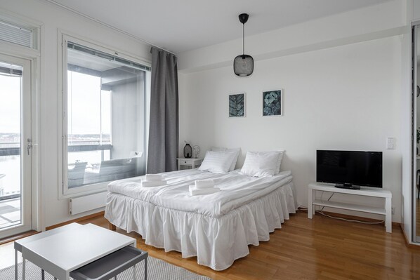 A modern bedroom with a large bed, a television, and a view of the city through the window. - Lake View 7th Floor Studio next to Downtown (Tampere)