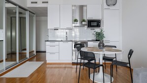 Una cucina moderna con mobili bianchi, un forno in acciaio inossidabile, un forno a microonde e un'area pranzo con un tavolo rotondo e sedie nere.