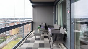 Un balcone con pavimento a scacchi, un divano, un tavolo con una pianta e vista su edifici e una strada.