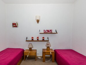 A room with two beds, a wall-mounted shelf with decorative items, a wall-mounted lamp, and a small picture frame.