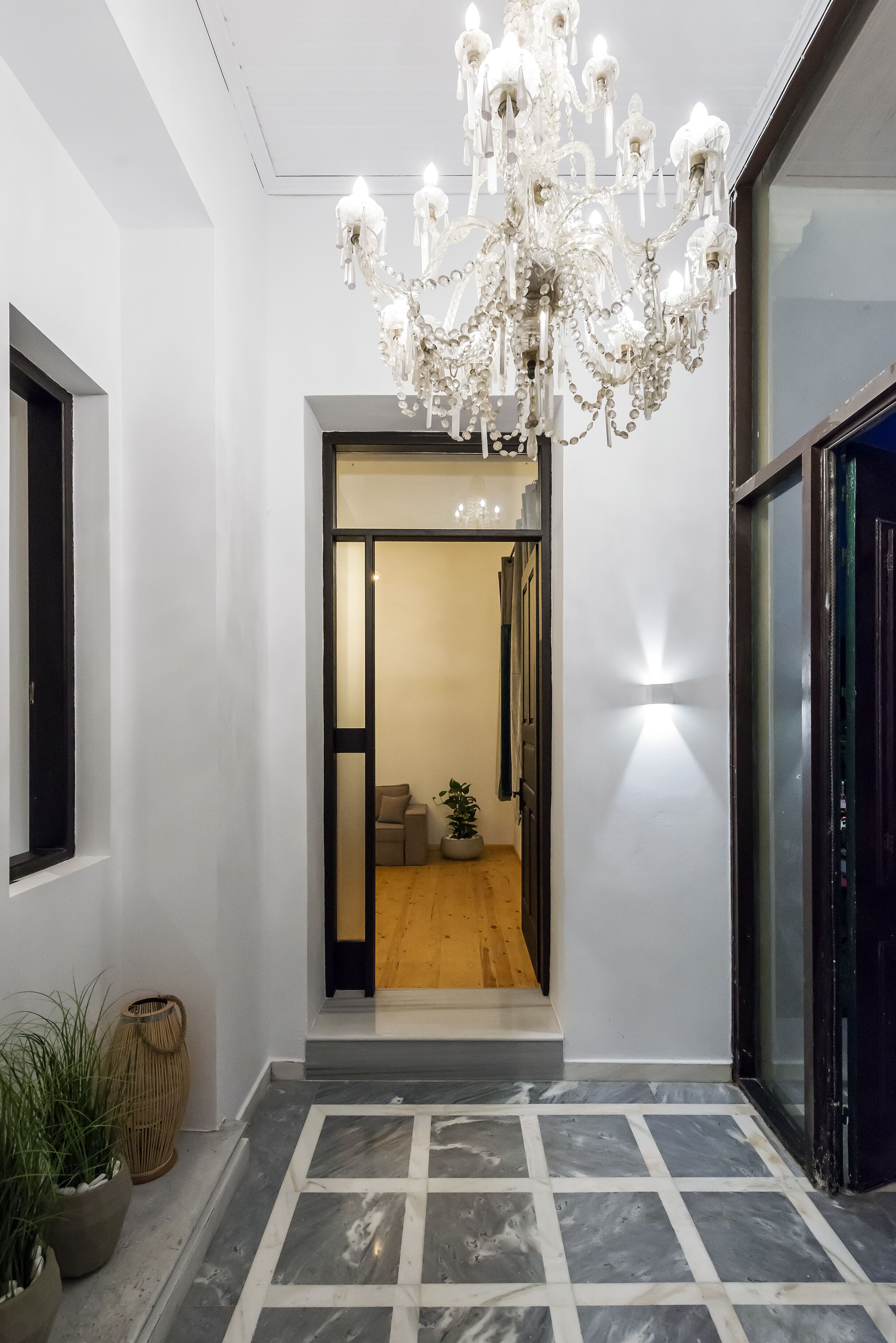 A modern interior with a chandelier, a glass door leading to a room, and a tiled floor.